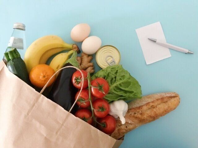紙袋から飛び出している野菜とそばにある紙とペン