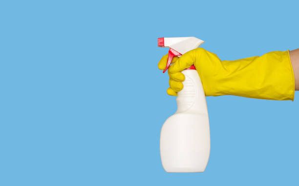 ゴム手袋をはめた手は、洗浄剤または消毒剤でスプレーガンを保持しています。テキスト用の独立した、青い背景、空きスペース。