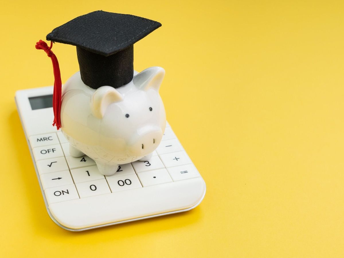 学生ローンの支払い計算、奨学金や学校や教育のコンセプトのための貯蓄、コピースペースと黄色の背景に電卓に卒業帽子をかぶって白い貯金箱