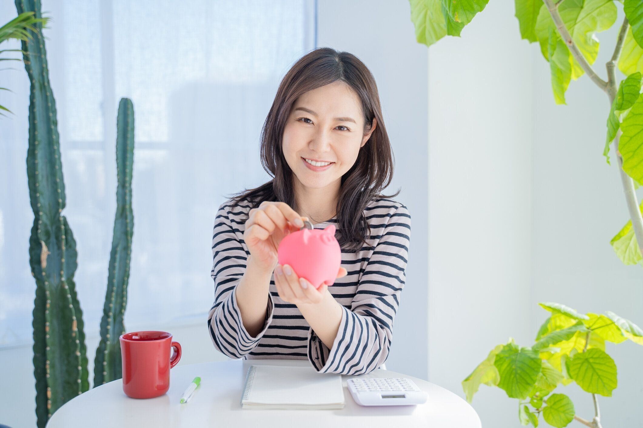 明るいリビングルームの貯金箱でお金を節約する女性。