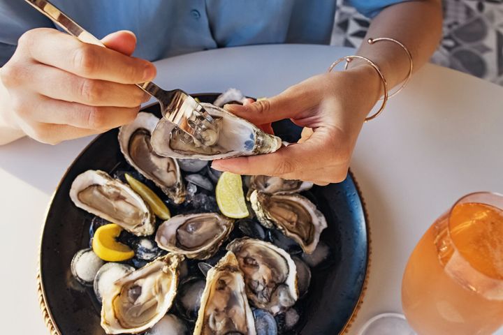 レモンのクローズアップで新鮮なカキを食べる女性。