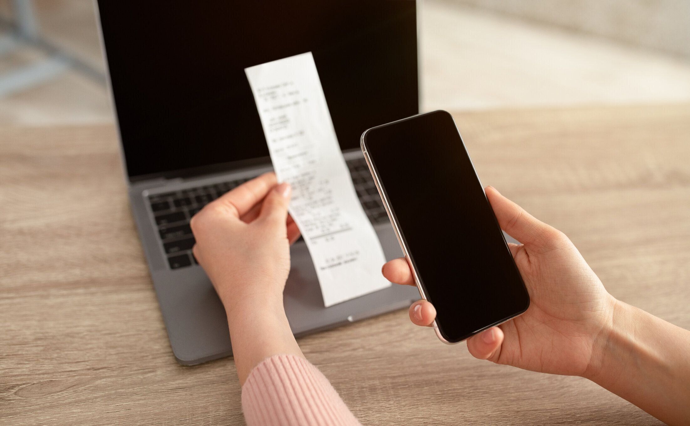 空の画面と紙幣やスリップでスマートフォンを持つ女性の手、机の上にラップトップを持つ職場に座っている