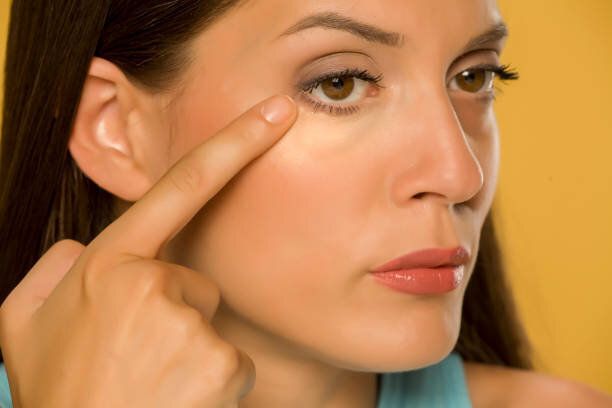 黄色の背景に彼女の低まぶたに触れる若い女性