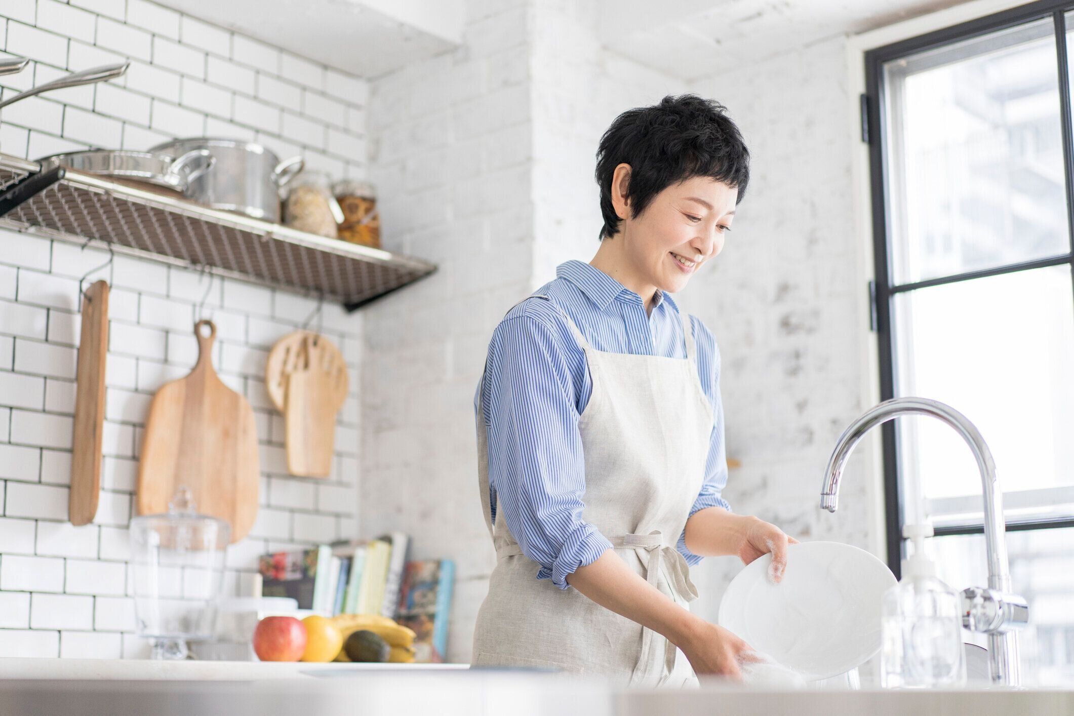 アジア人女性が台所で皿を洗っている。