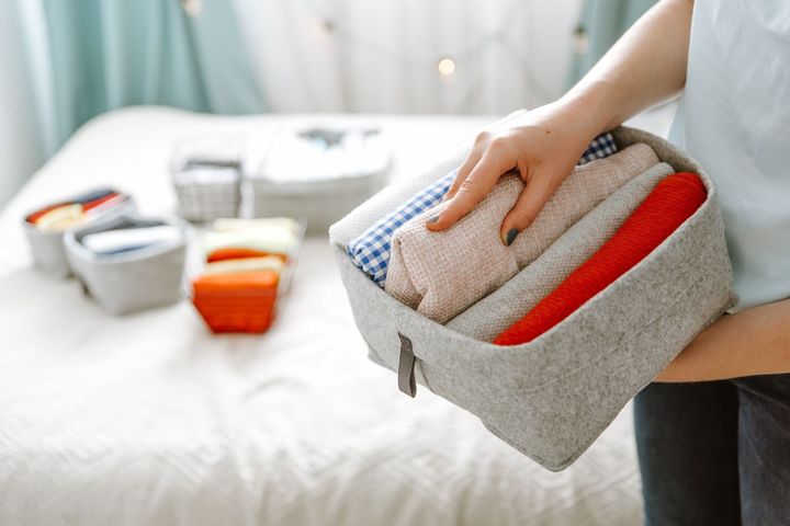 ワードローブで服を整理し、箱にシャツを入れ、バスケットを棚に入れる女性。洗濯後はきちんと折りたたまれた服。ミニマリストライフスタイルのコンセプト