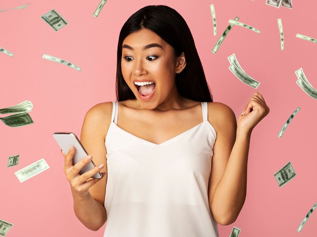 ビッグウィン。ドルマネーシャワーの下でスマートフォンで勝利を祝うアジアの女の子