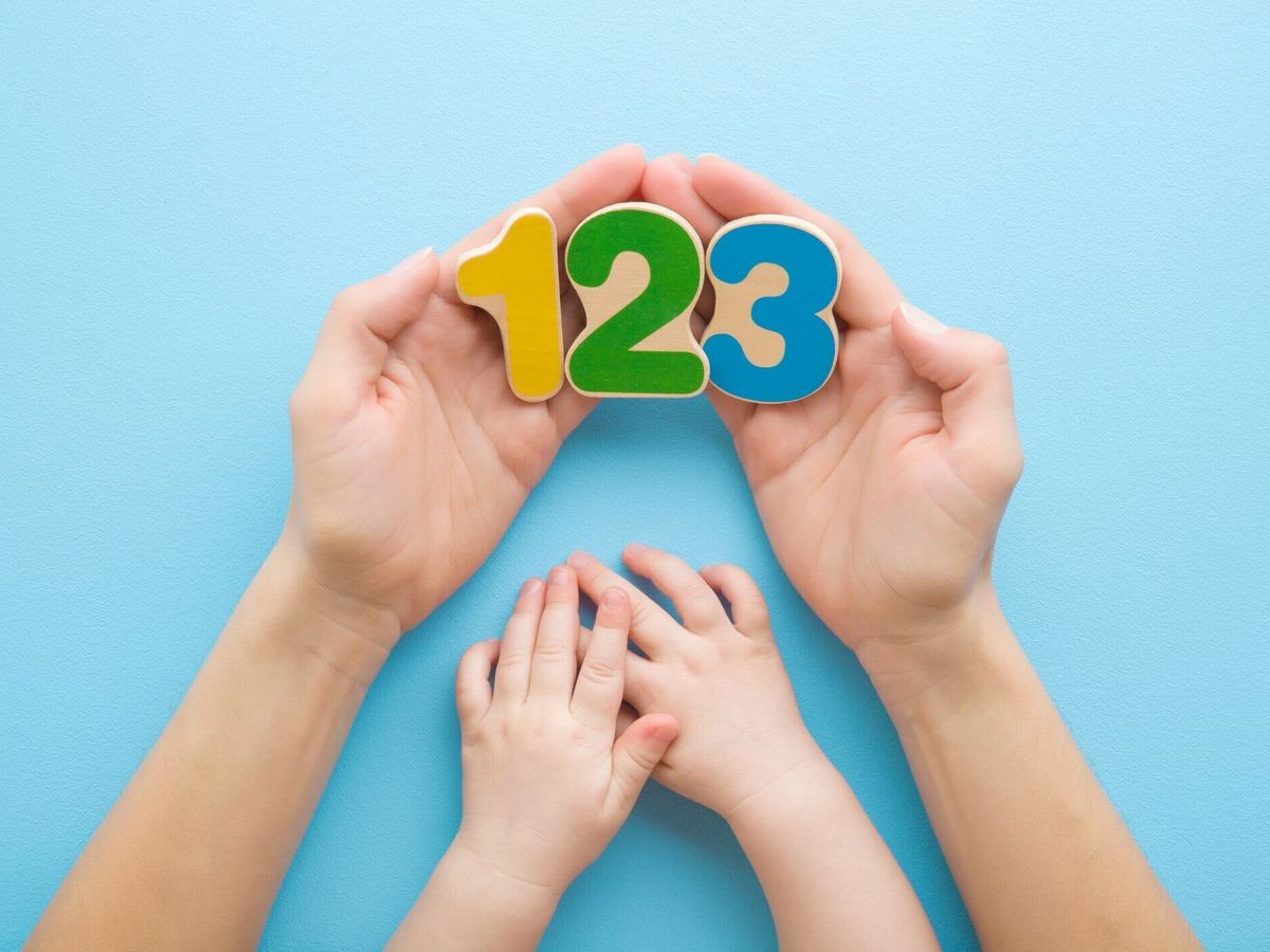 水色のテーブルの背景に赤ちゃんにカラフルな木製の数字を示す若い大人の母親の手。パステルカラー。学ぶ時間。視点ショット。クローズ アップ。トップダウンビュー。