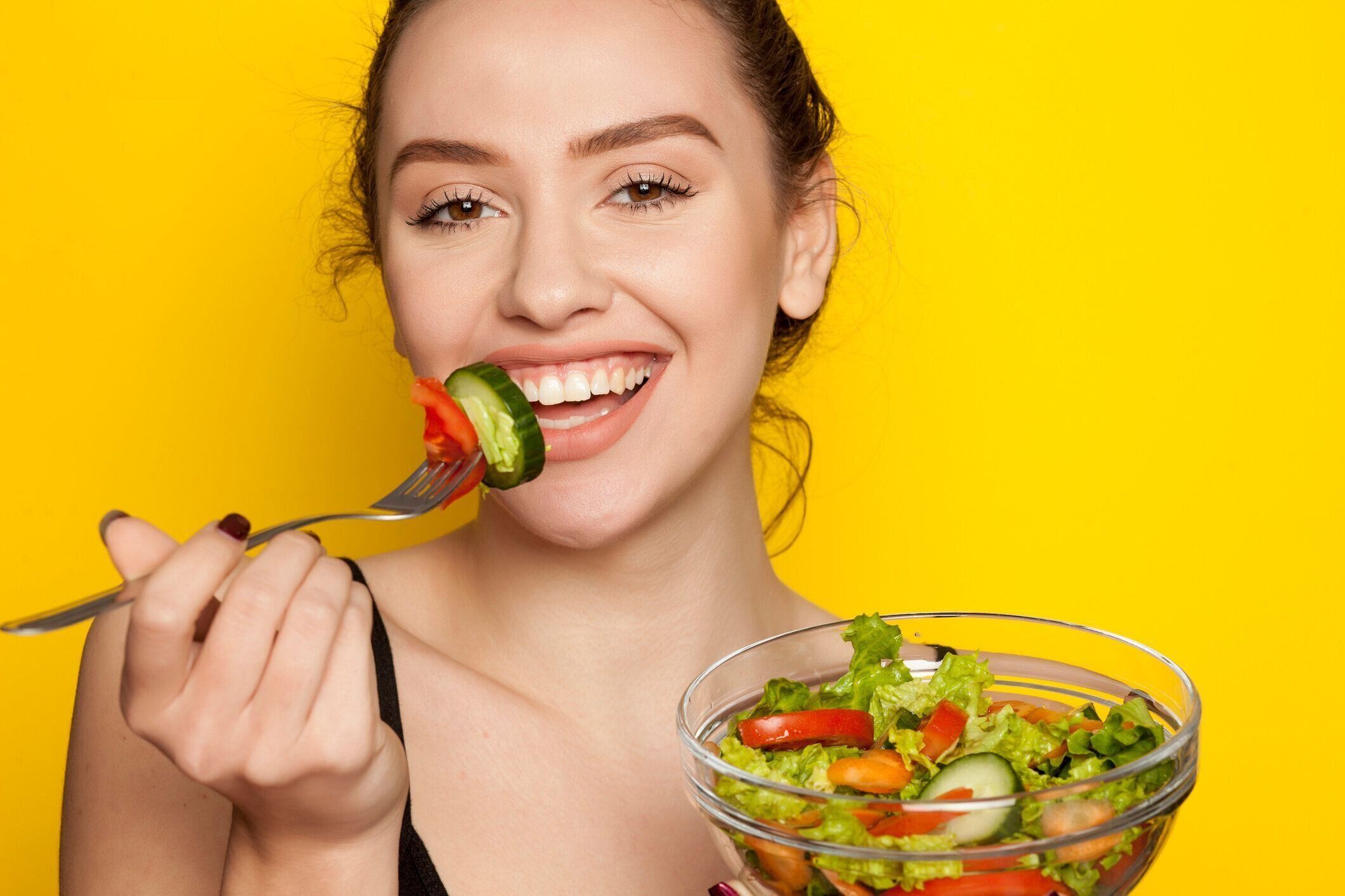 黄色の背景でサラダを食べる若い美しい女性