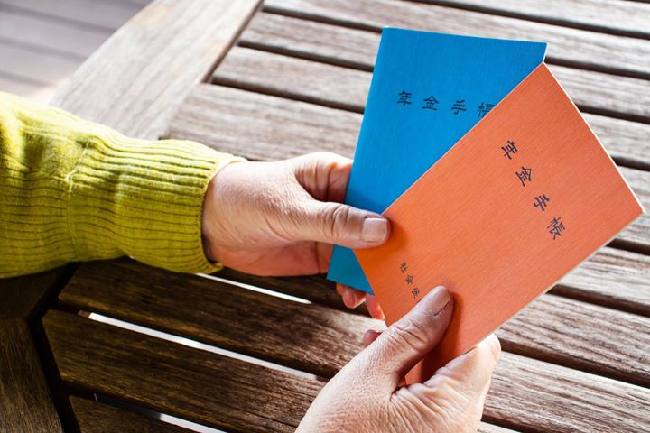 女性が手に持っている本のタイトルは「年金ハンドブック」です。