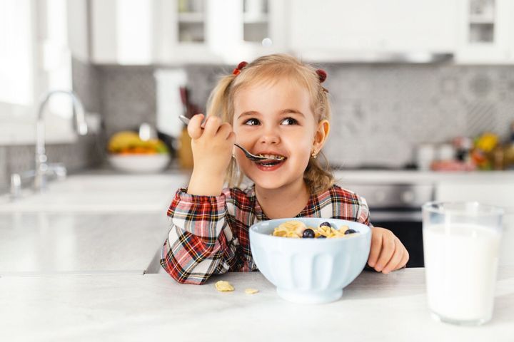 キッチンでシリアル、牛乳、ブルーベリーと朝食を持つ美しい小さな女の子