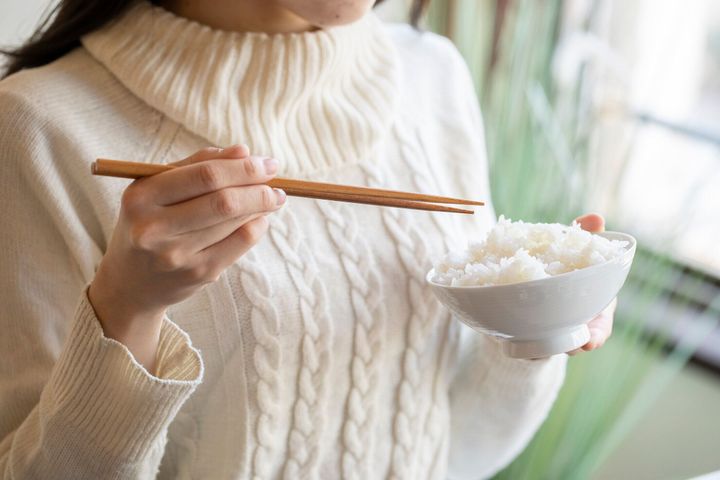 白いご飯と箸をボウルに入れておる女性