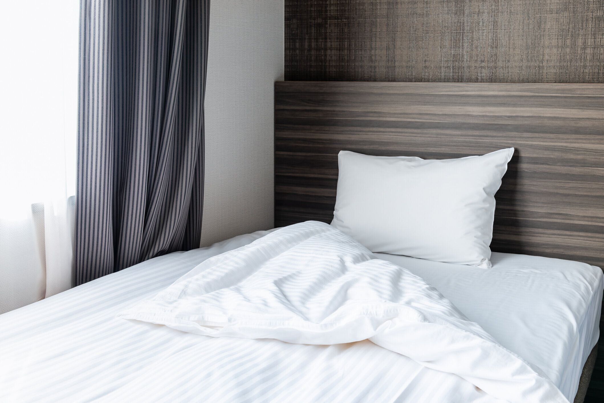 寝室の窓際のベッドに白い枕と白い毛布。散らかったベッドと寝室のコンセプト。