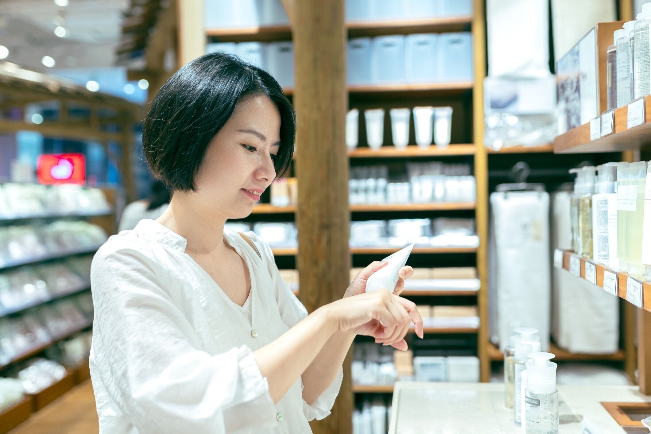 店内の化粧品売り場でハンドクリームを試すアジアンガール