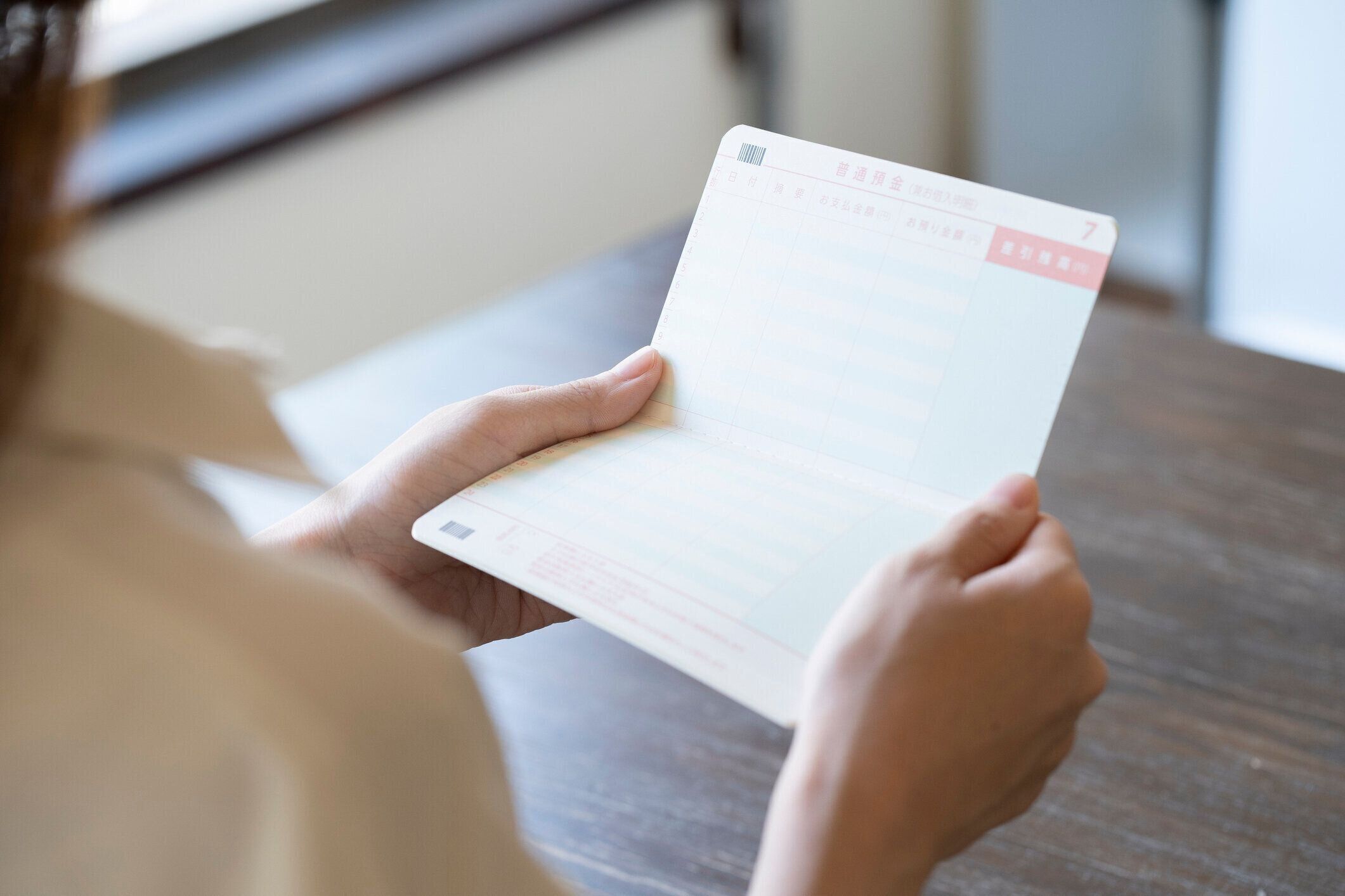 机の上で通帳を開こうとする若い女性