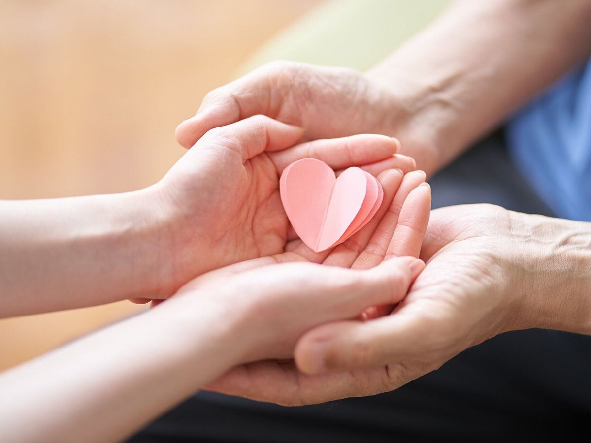 ハート型の物を持つ介護者と高齢者の手