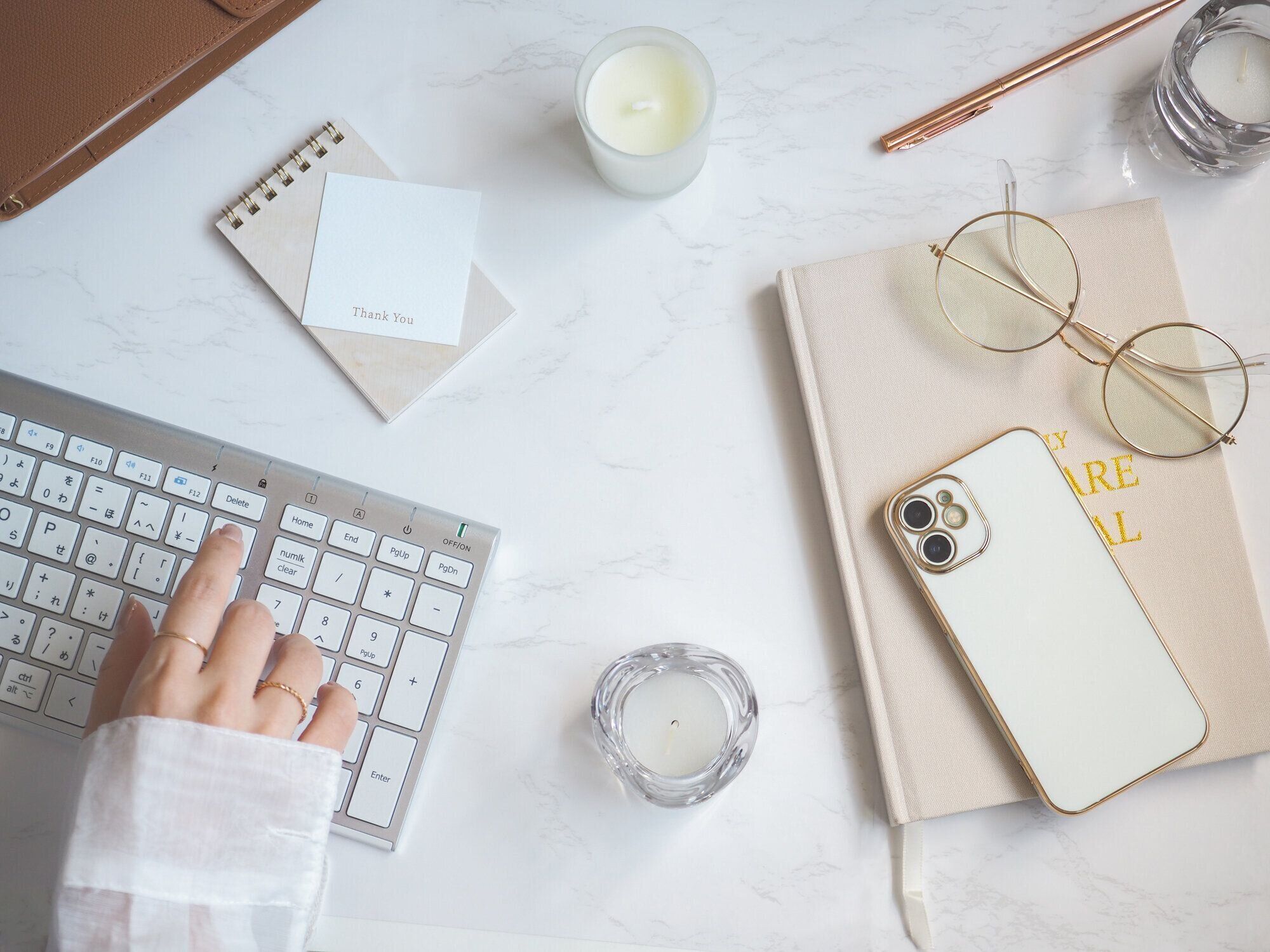 明るく清潔な女性の机、ラップトップとコンピューターのキーボードで入力する女性の手の上から見た図