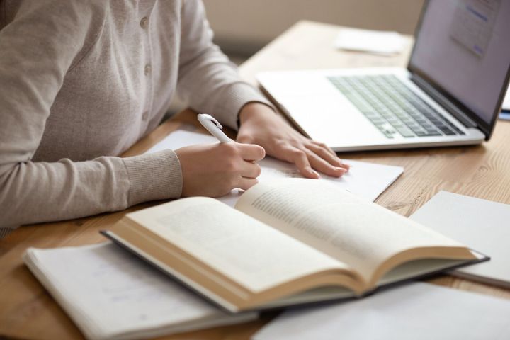 開いた教科書からメモを書き留めた女子学生をクローズアップ。