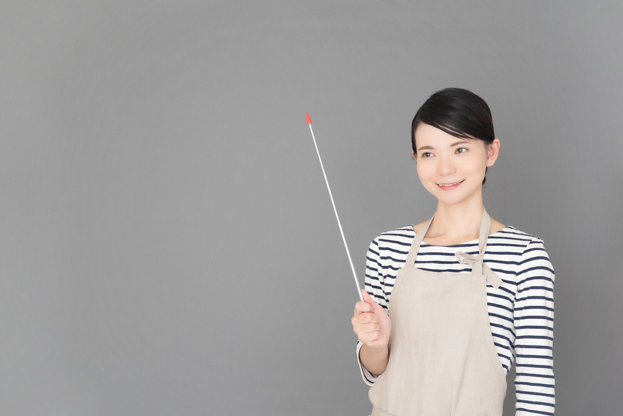 灰色の背景の前に立つエプロンの女性