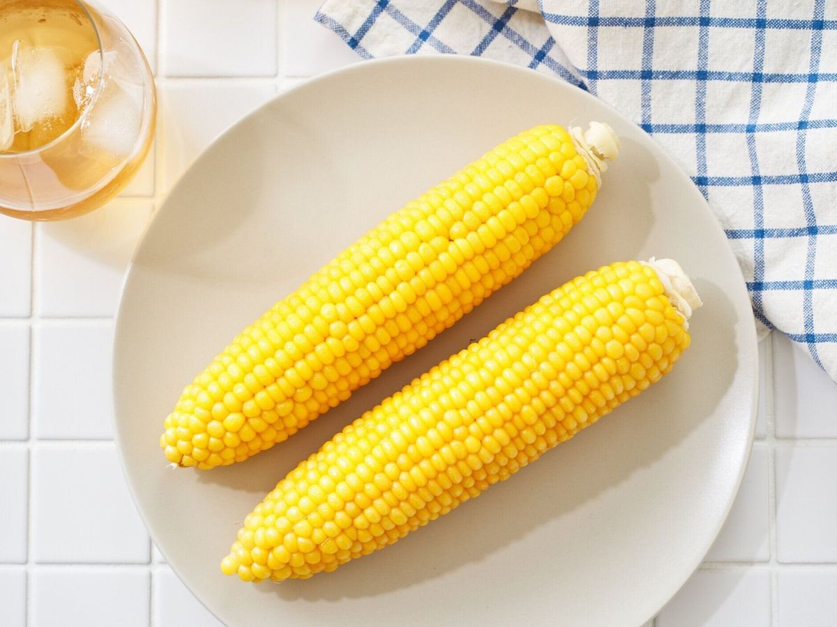 穂軸の上のシンプルな茹でたトウモロコシを皿に盛り付けます。