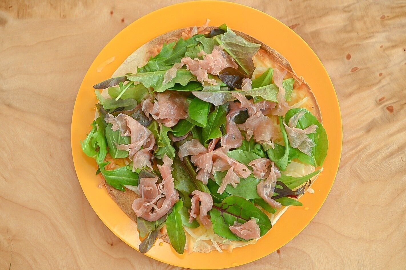 黄色い皿に盛られた生ハムとベビーリーフのピザ