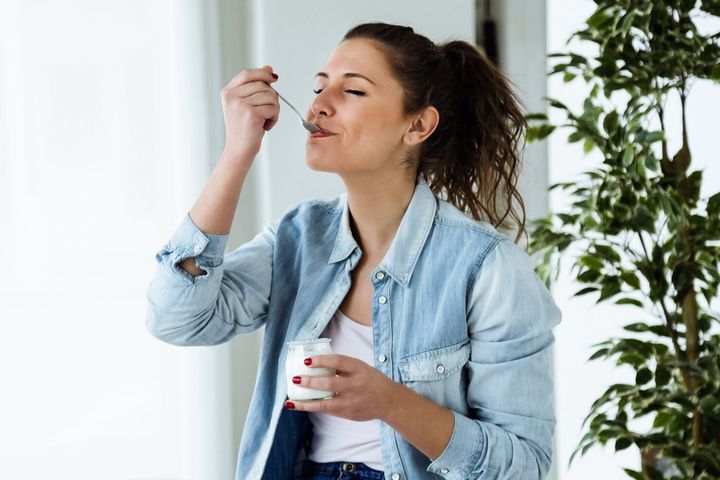 美しい若い女性自宅で食べるヨーグルトます。