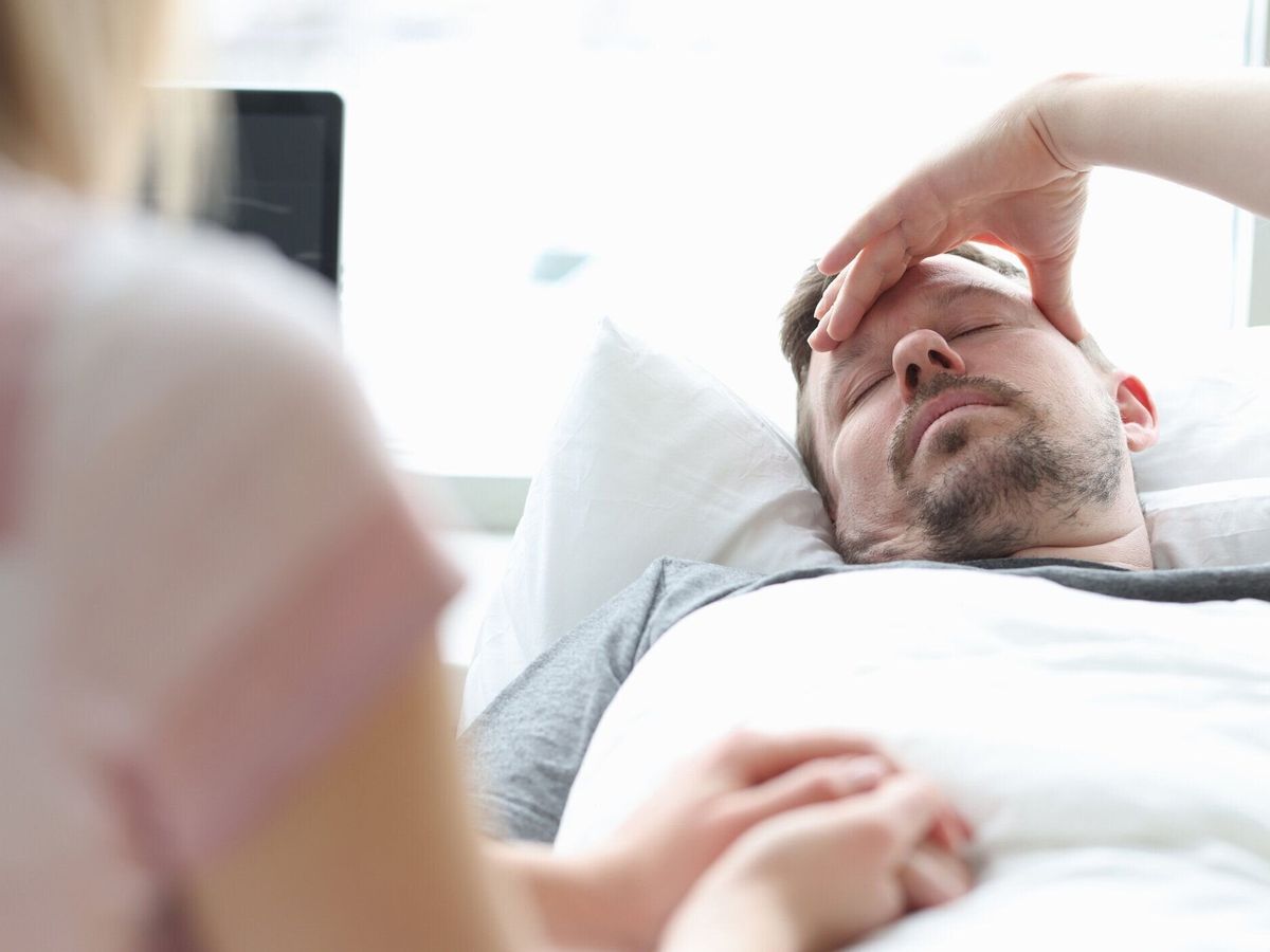 病室で病気の男性の手を握る女性の訪問者