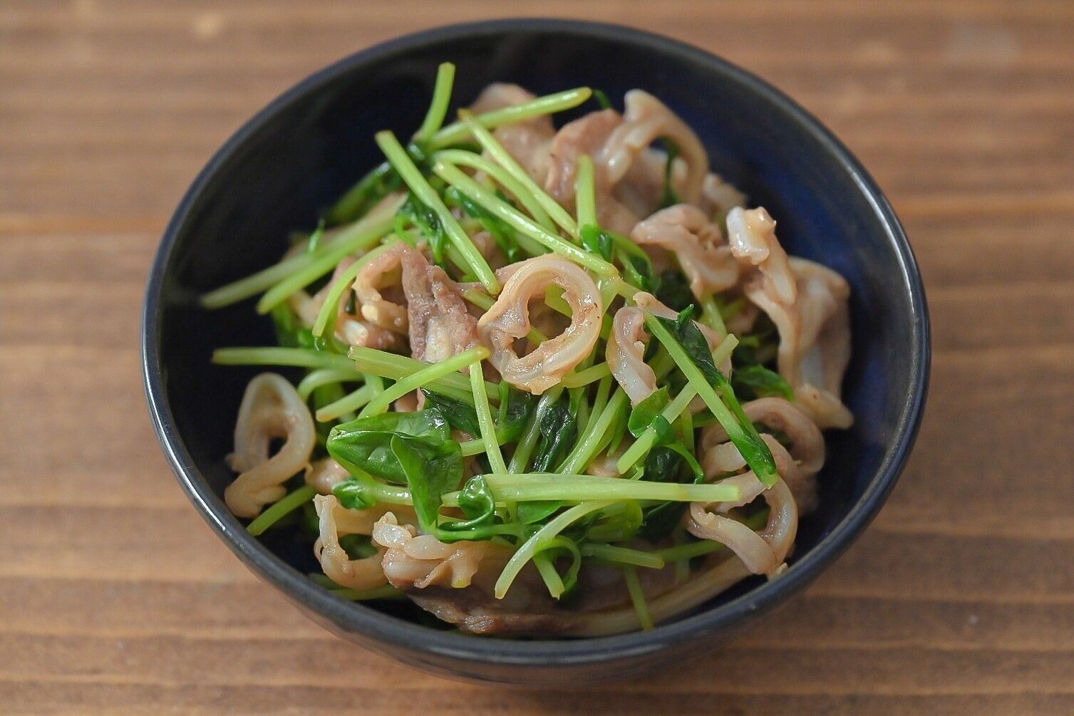 青い皿に盛られた豚軟骨と豆苗炒め