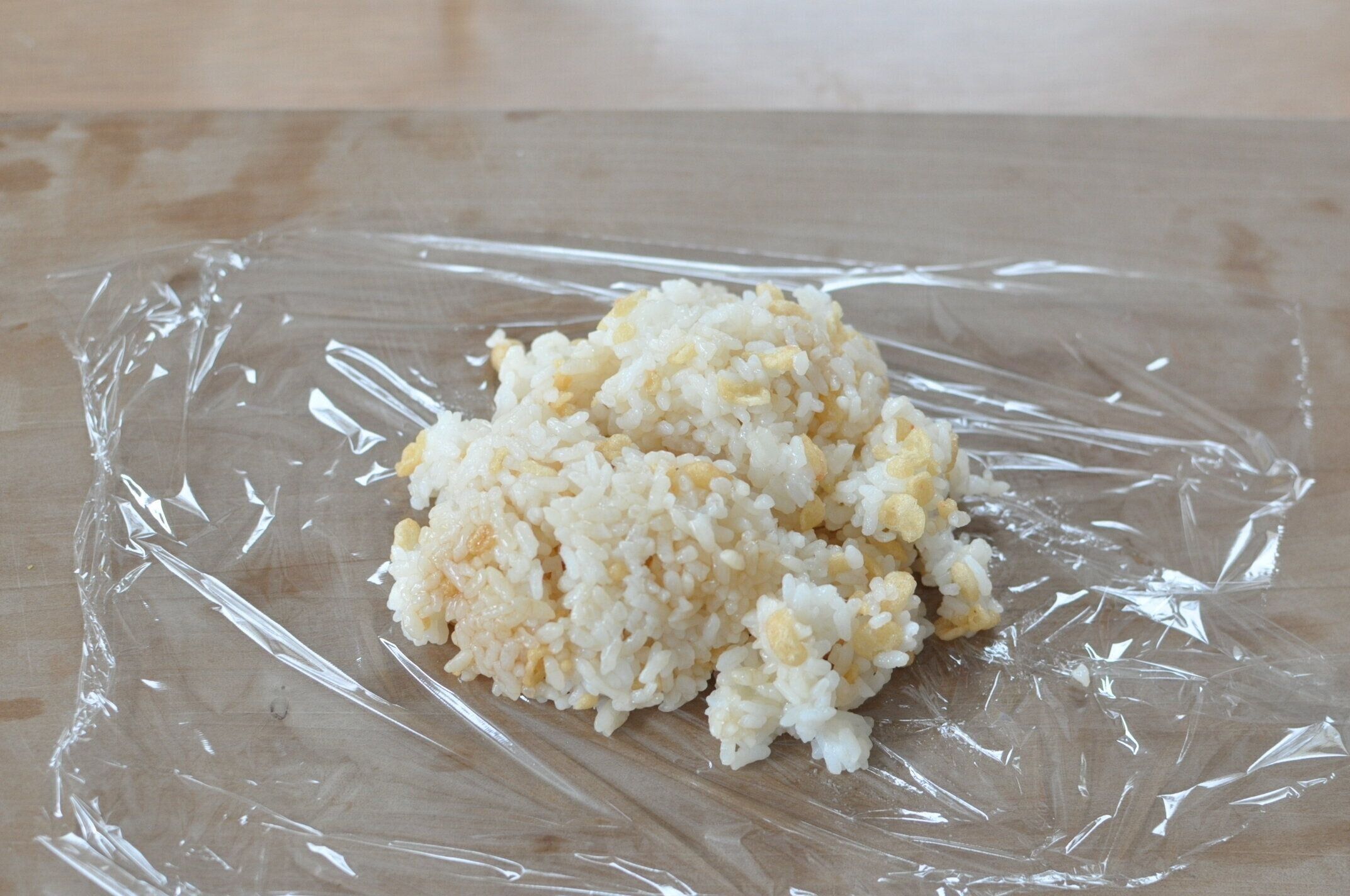 広げたラップの上に、揚げ玉と麺つゆを混ぜたご飯をのせた様子