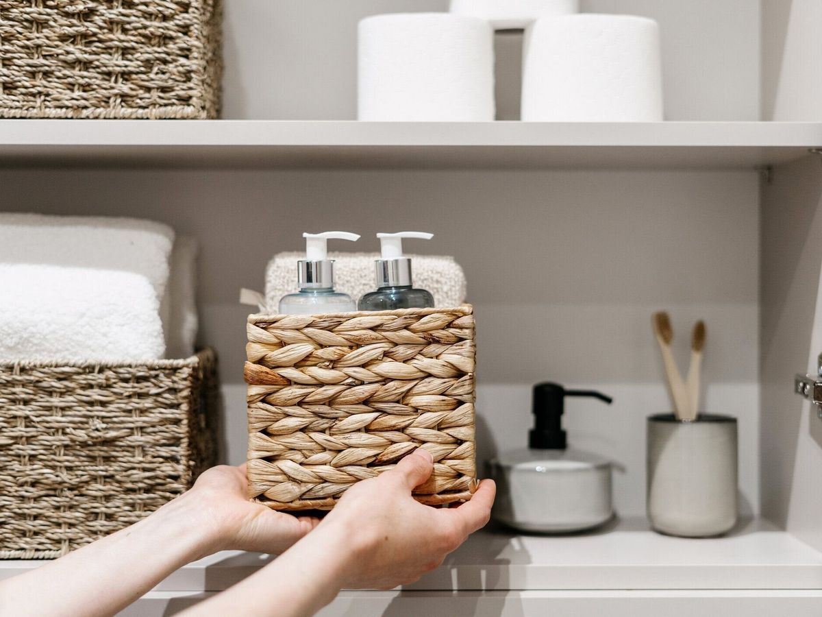 女性はバスルームのクローゼットに化粧品を入れた籐箱を置く