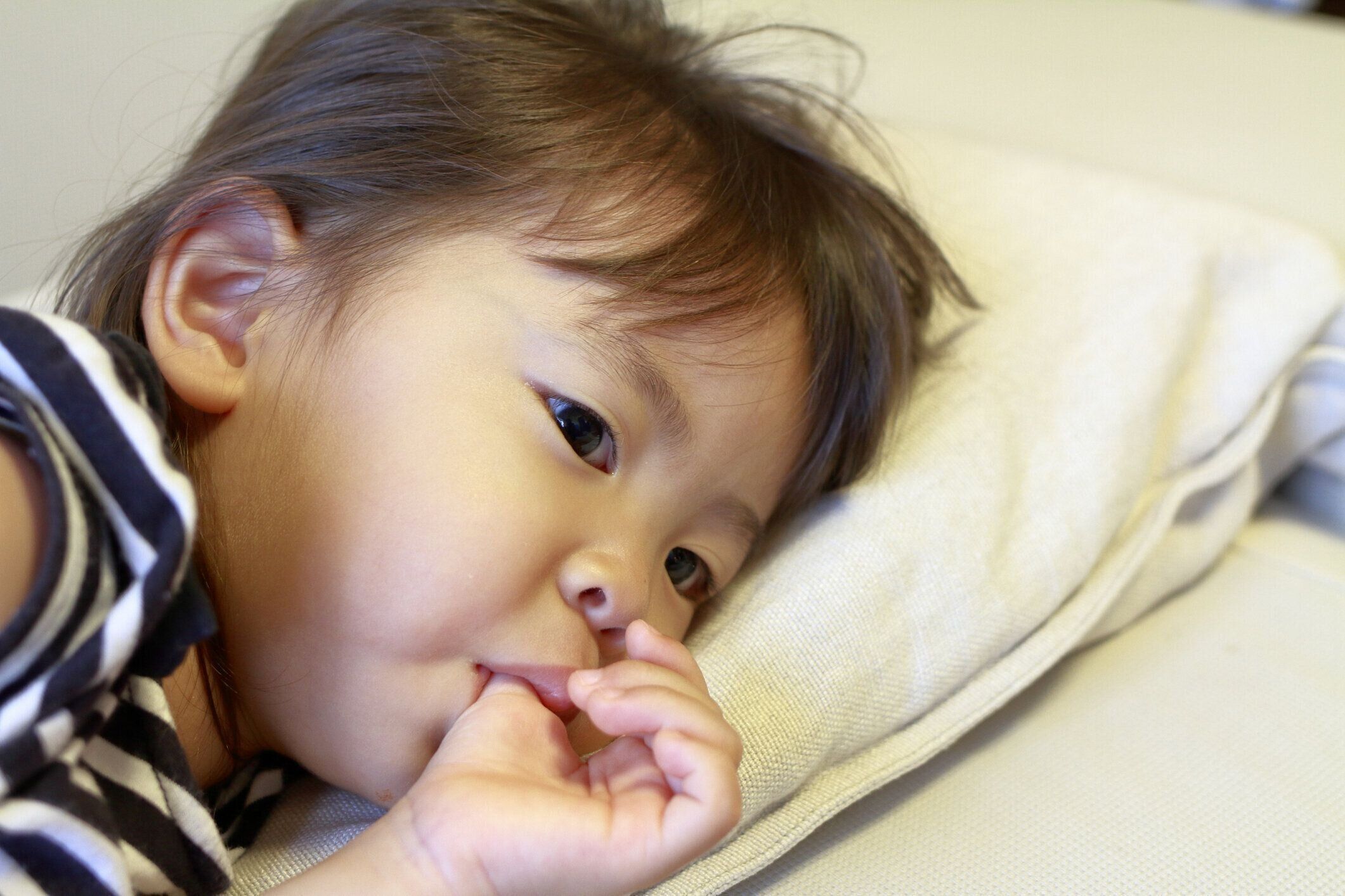 (2 歳) 彼女の指をしゃぶりで日本人の女の子を横になっています。