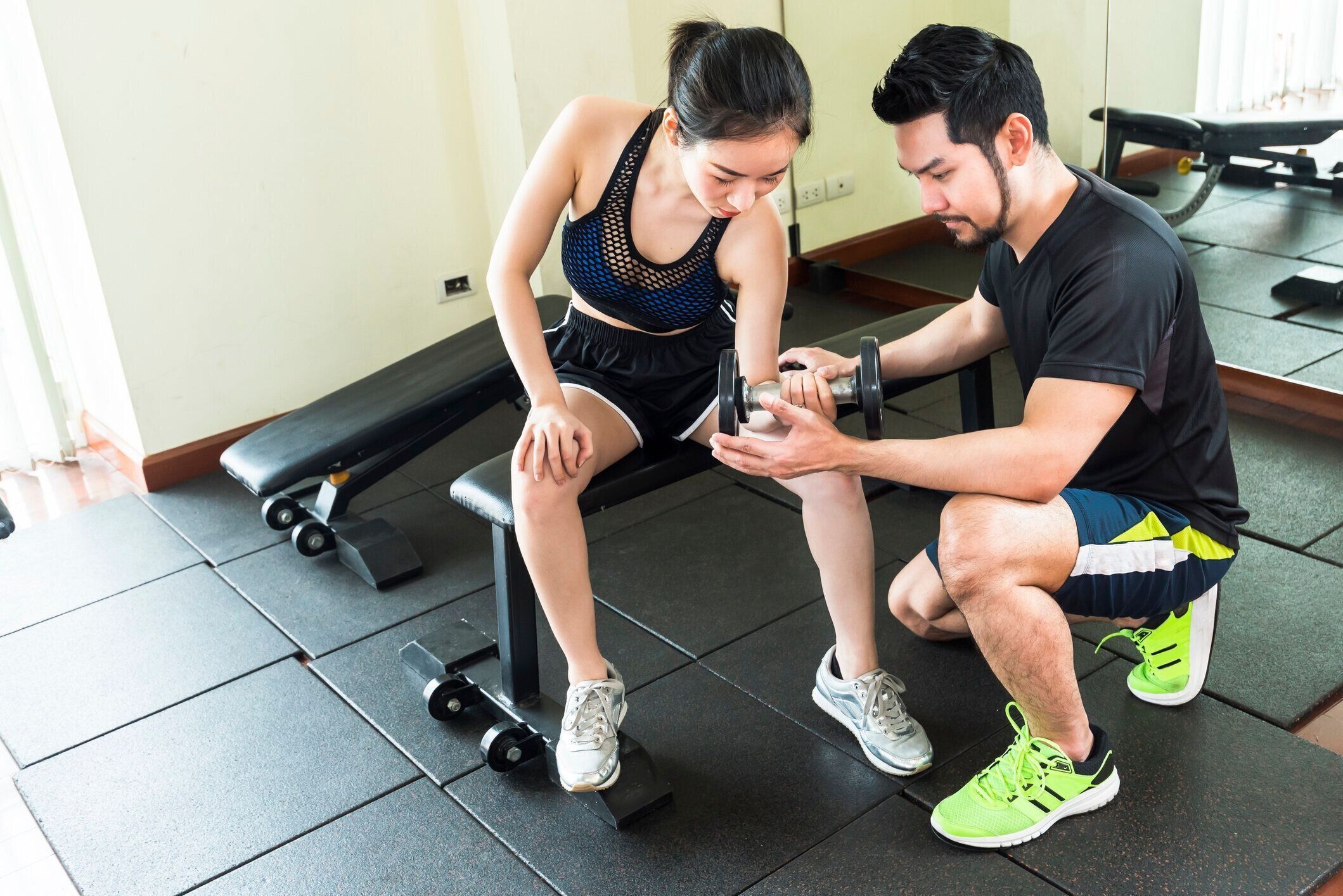 男性トレーナーの世話をしている女性は、フィットネスでダンベルを持ち上げています。