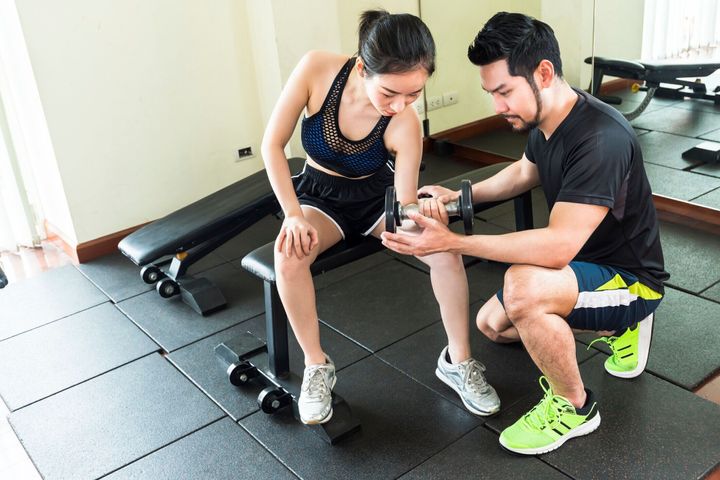 男性トレーナーの世話をしている女性は、フィットネスでダンベルを持ち上げています。