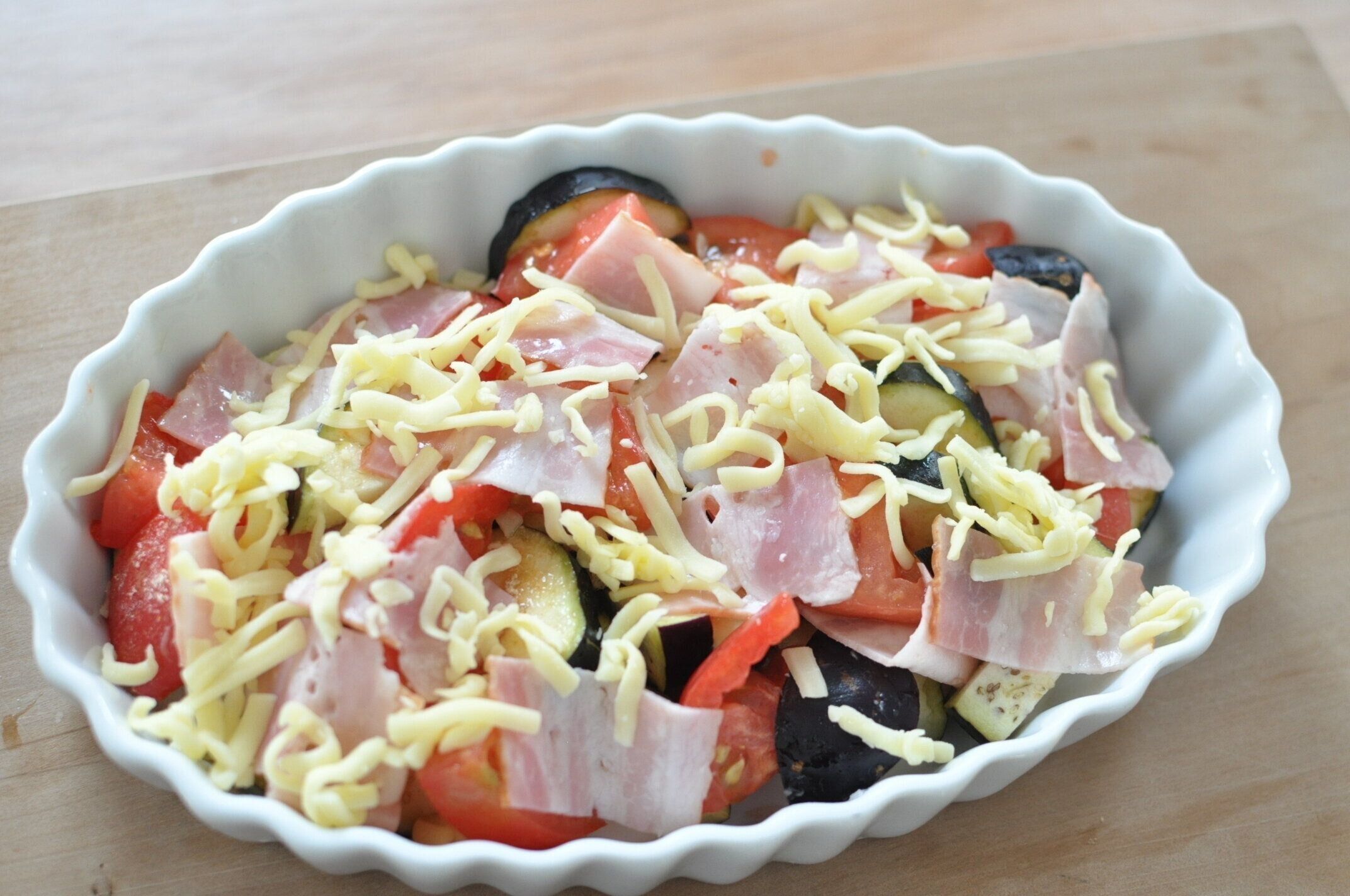 耐熱皿に、なす、トマト、コンソメ、ベーコン、チーズを入れた様子