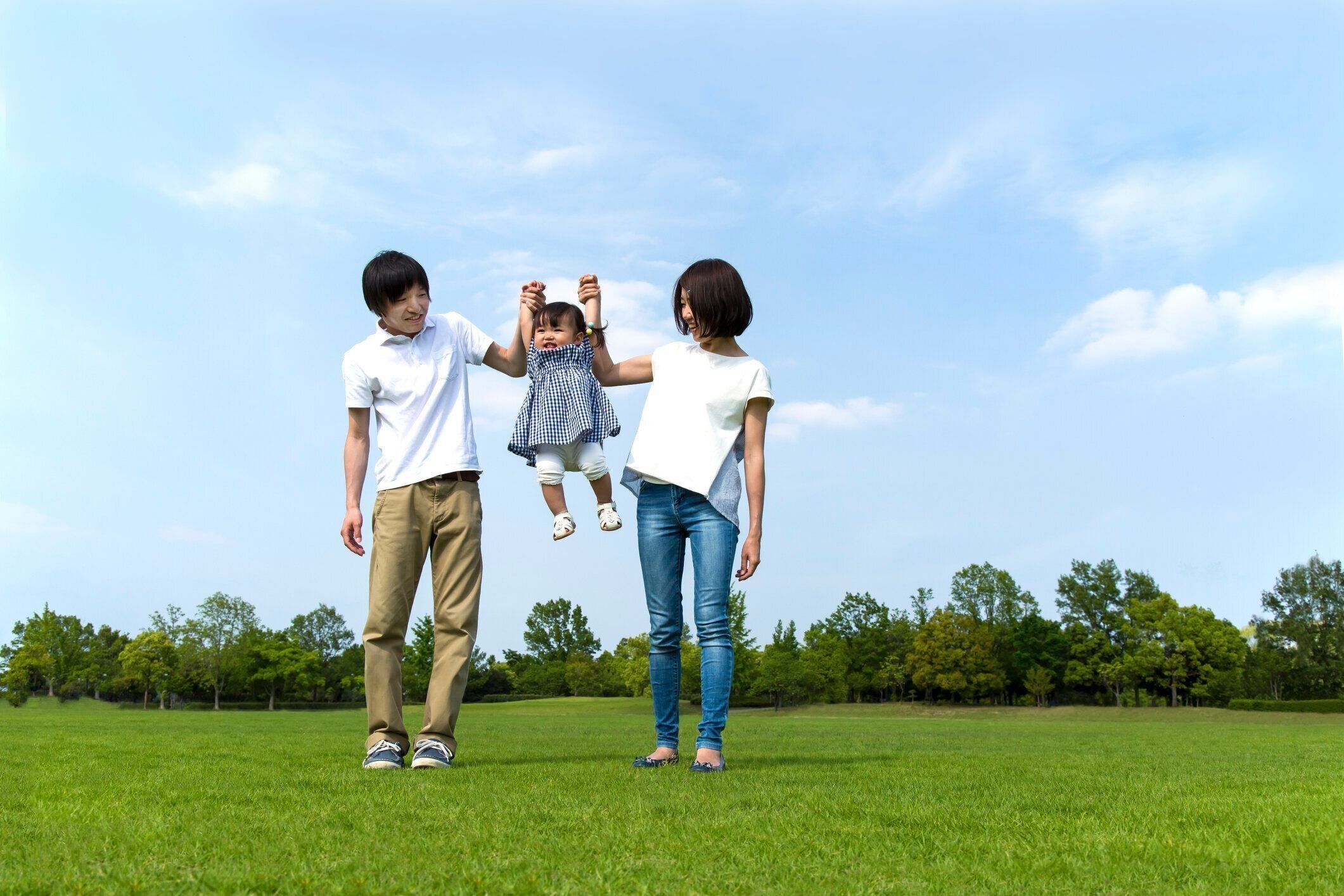 青空に対して緑の草の広場で遊ぶ両親と小さな娘