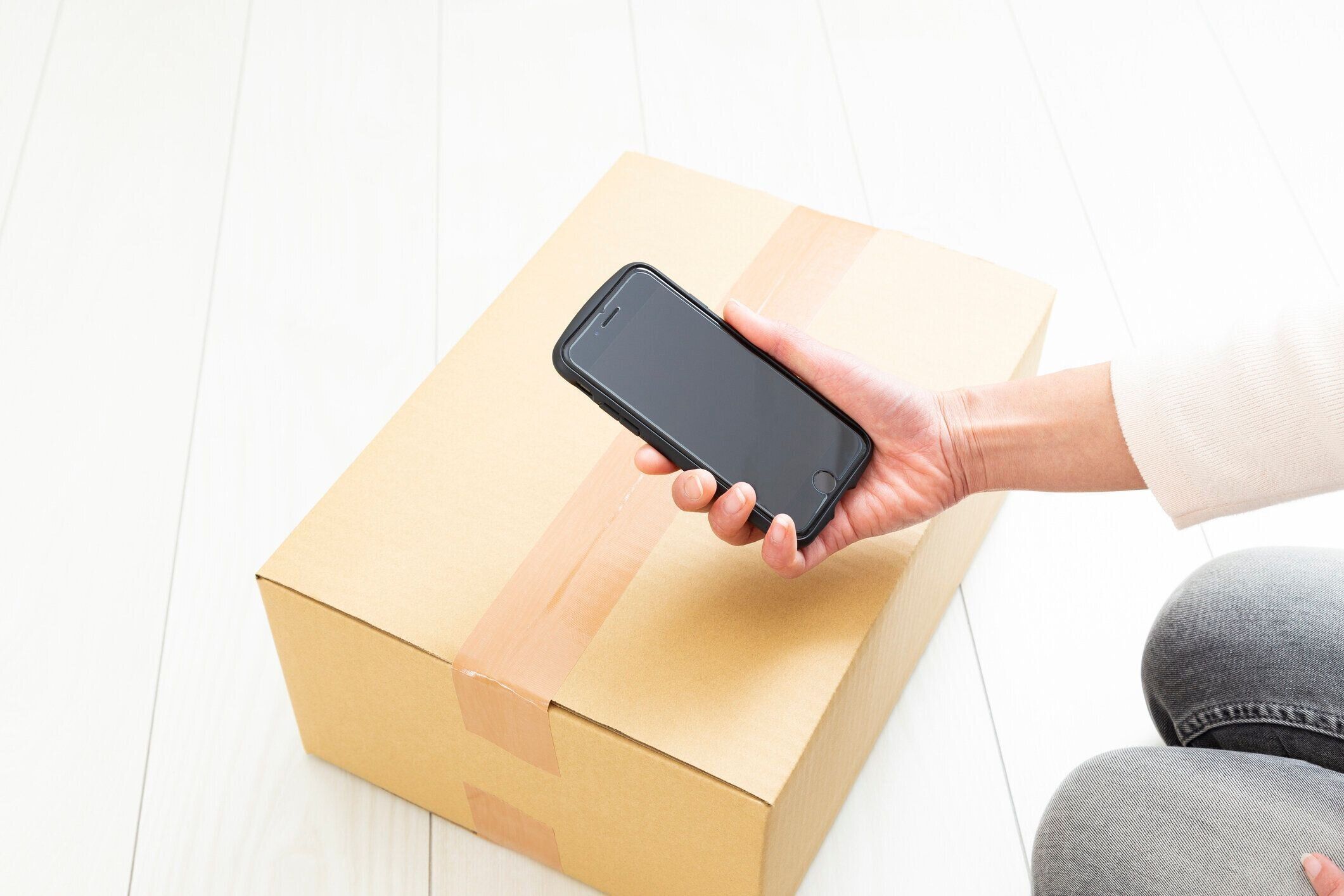 女性の手がスマートフォンで箱の写真を撮る。