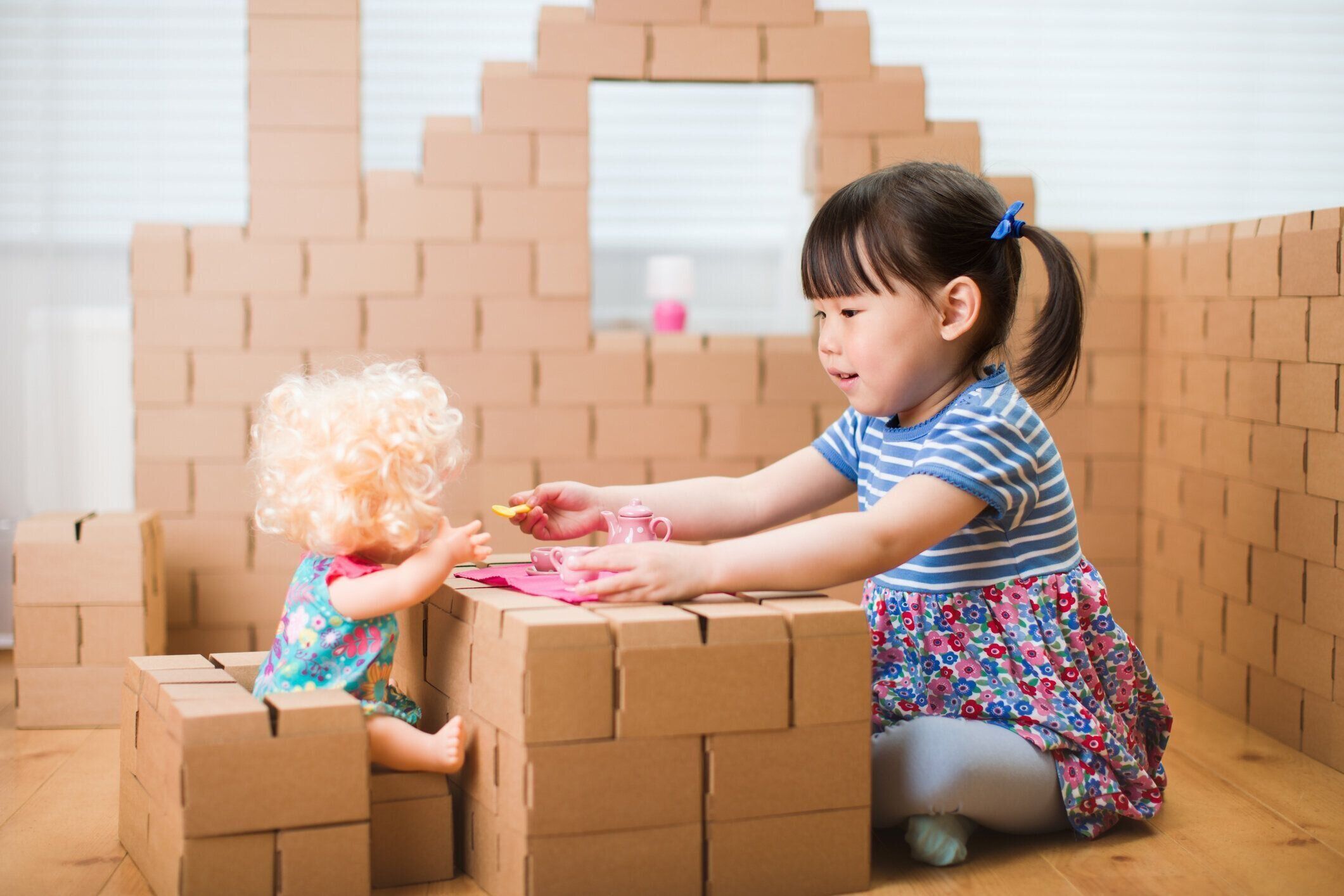 幼児の女の子は段ボールブロックの家で赤ちゃんのケアをプレイふりをする