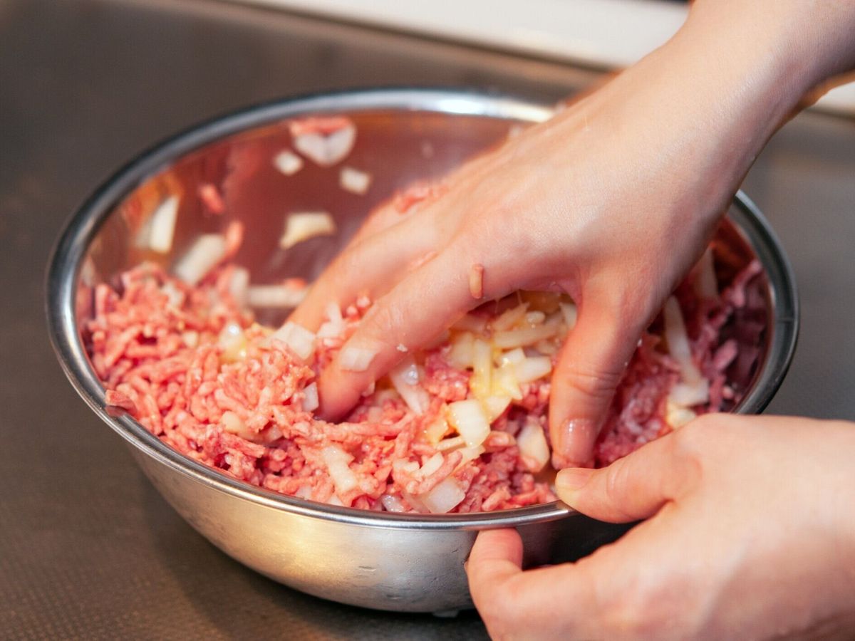 ボウルにハンバーガーを調理するためのひき肉や他の材料を混合する女性の手。