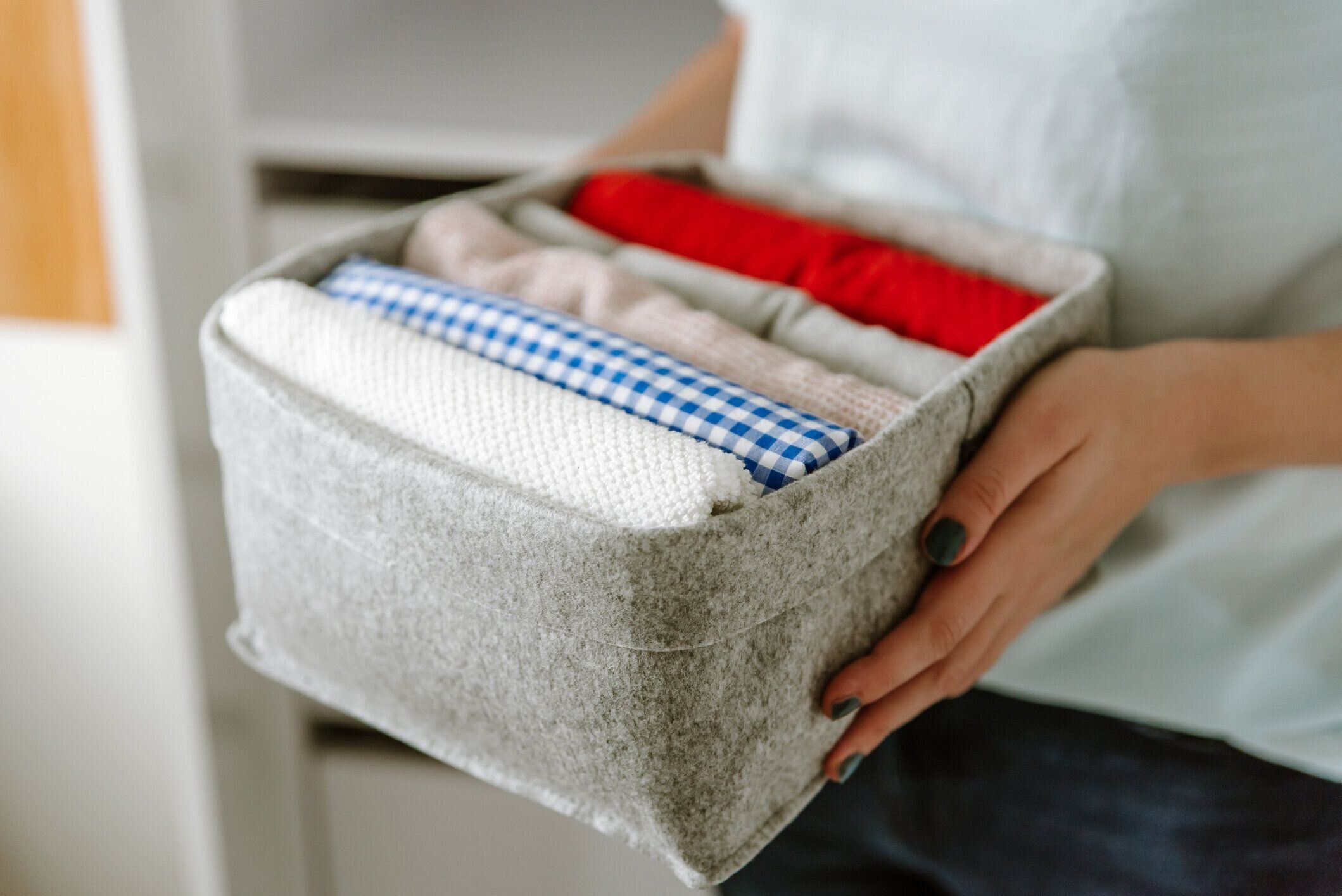 ワードローブで服を整理し、箱にシャツを入れ、バスケットを棚に入れる女性。洗濯後はきちんと折りたたまれた服。ミニマリストライフスタイルのコンセプト
