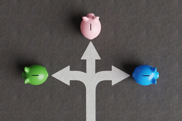 アスファルトに白い分割された道路標識と、異なる方向に向かう3つの異なる色の貯金箱。ストックピックとさまざまな投資商品の概念の図