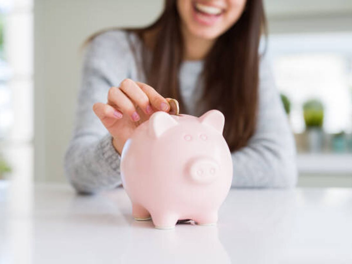 投資のための貯蓄として貯金としてピギーバンクの中にコインを入れて微笑む若い女性