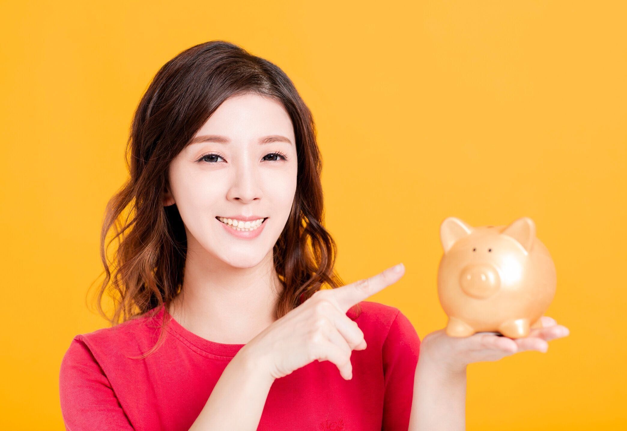黄色の背景に貯金箱を持つ若い女性
