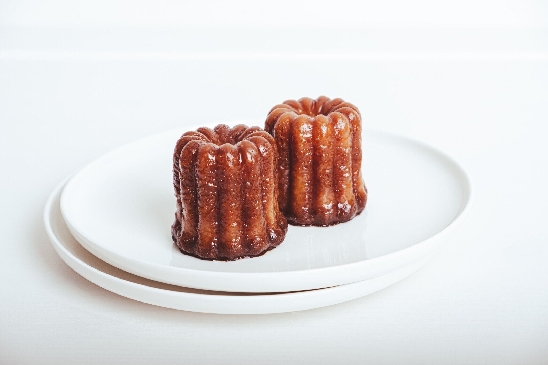 白い背景に白い皿にキャラメリゼした皮を持つおいしい焼きたてのカヌレ、ラム酒、バニラ風味のフレンチペストリー、接写。フランスのボルドー地方の名物。