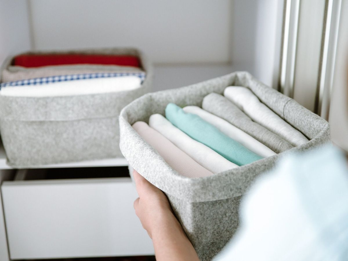 ワードローブで服を整理し、箱にシャツを入れ、バスケットを棚に入れる女性。洗濯後はきちんと折りたたまれた服。ミニマリストライフスタイルのコンセプト