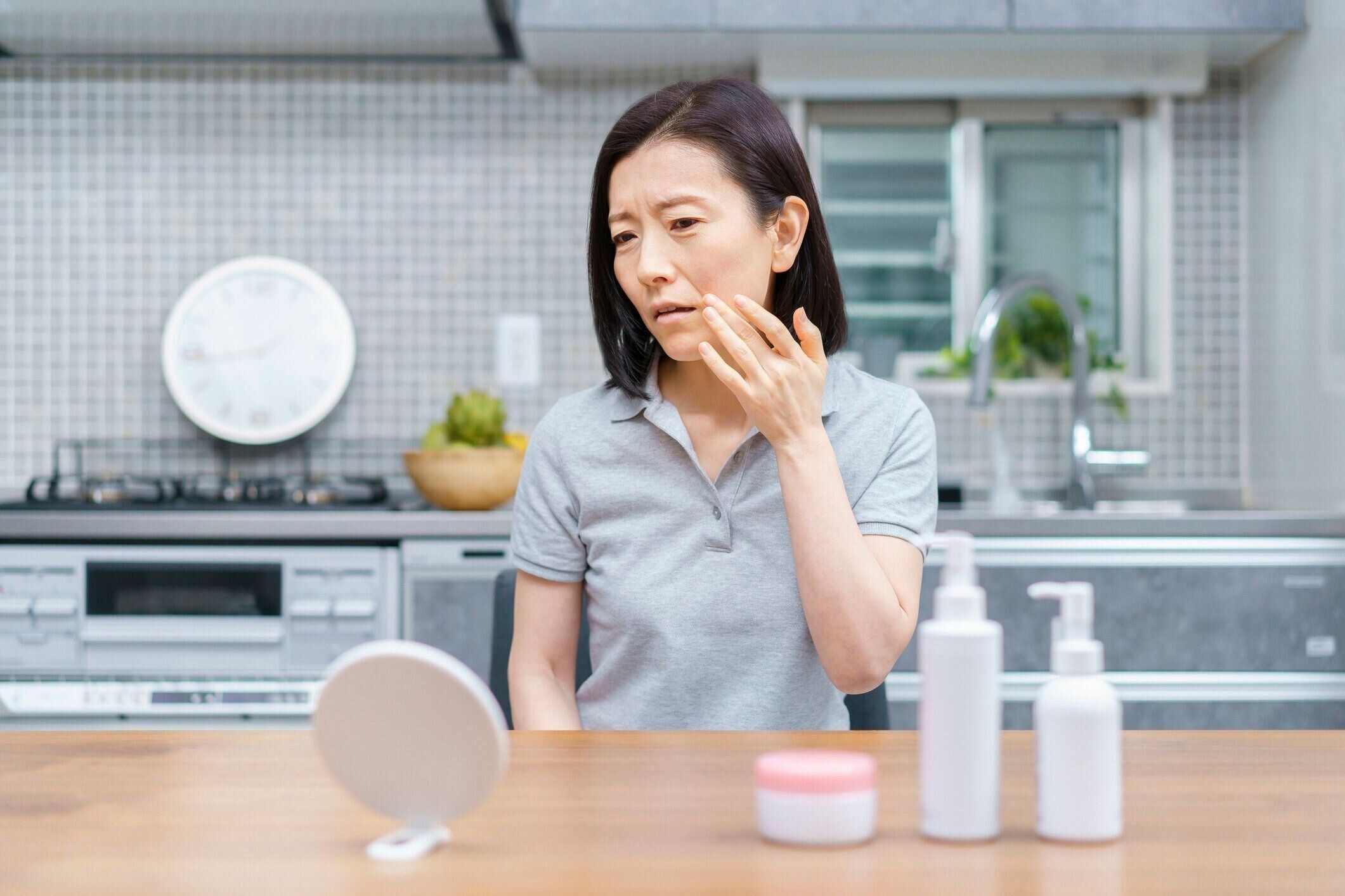 不安な表情で肌の状態をチェックする中年女性