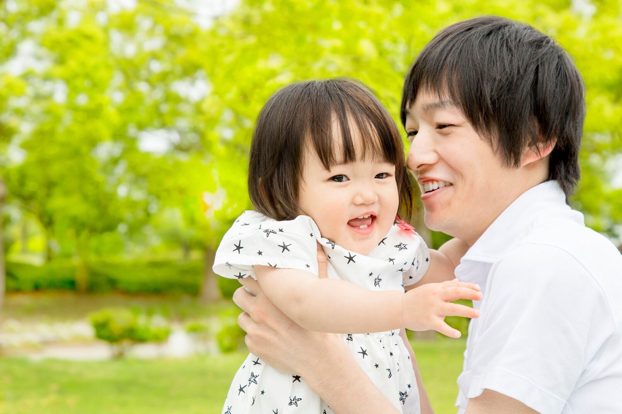 小さな女の子と緑の木の背景で遊んでいる父親