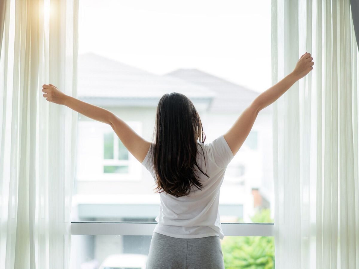 自宅の寝室で目を覚ました後、窓の近くで手と体を伸ばすアジアの女性の背面図。幸せで新しい一日を始めるコンセプト。若い幸せな働く女性の生活
