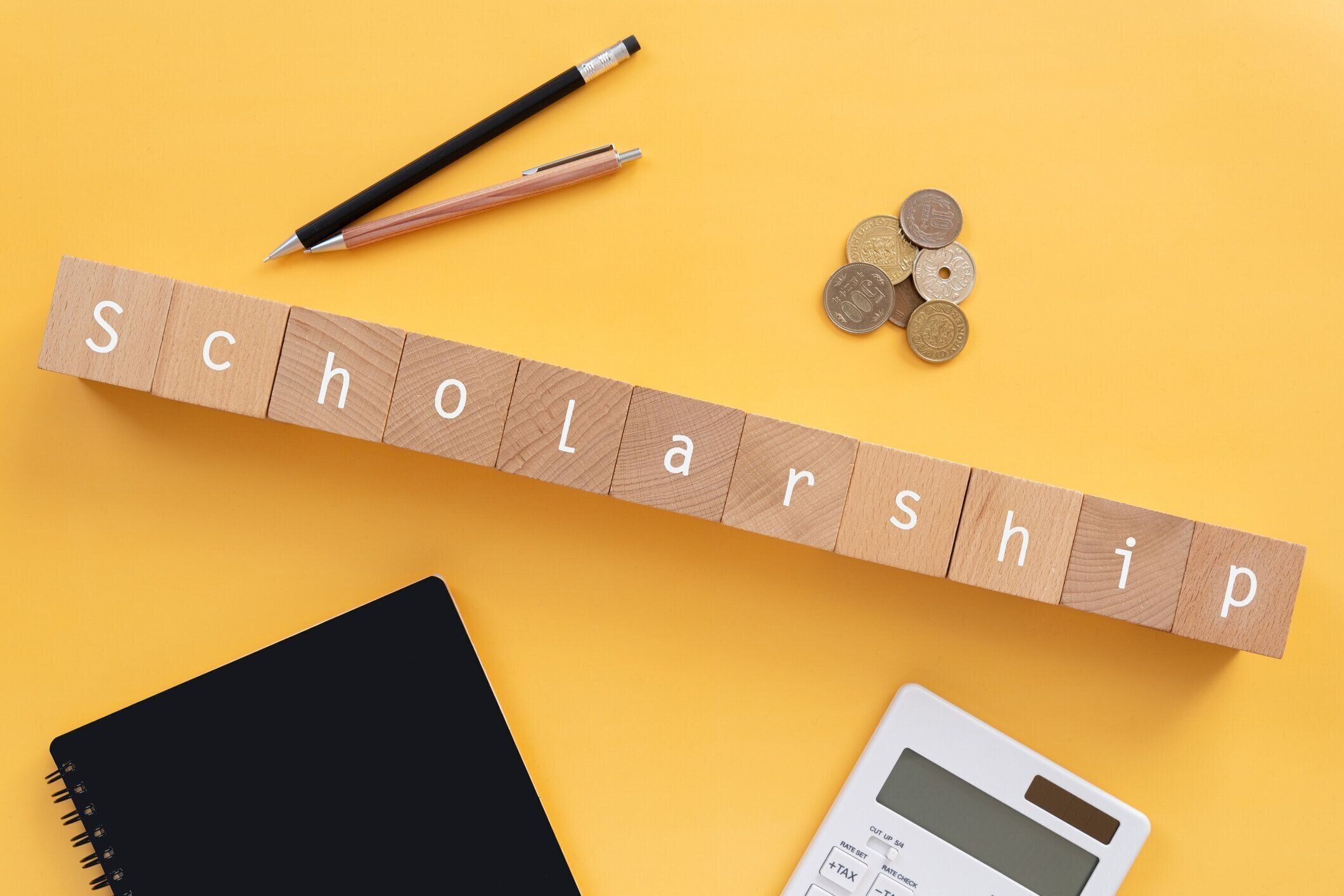 奨学金;コンセプト、ペン、メモ、コイン、電卓の「奨学金」テキストを持つ木製のブロック。