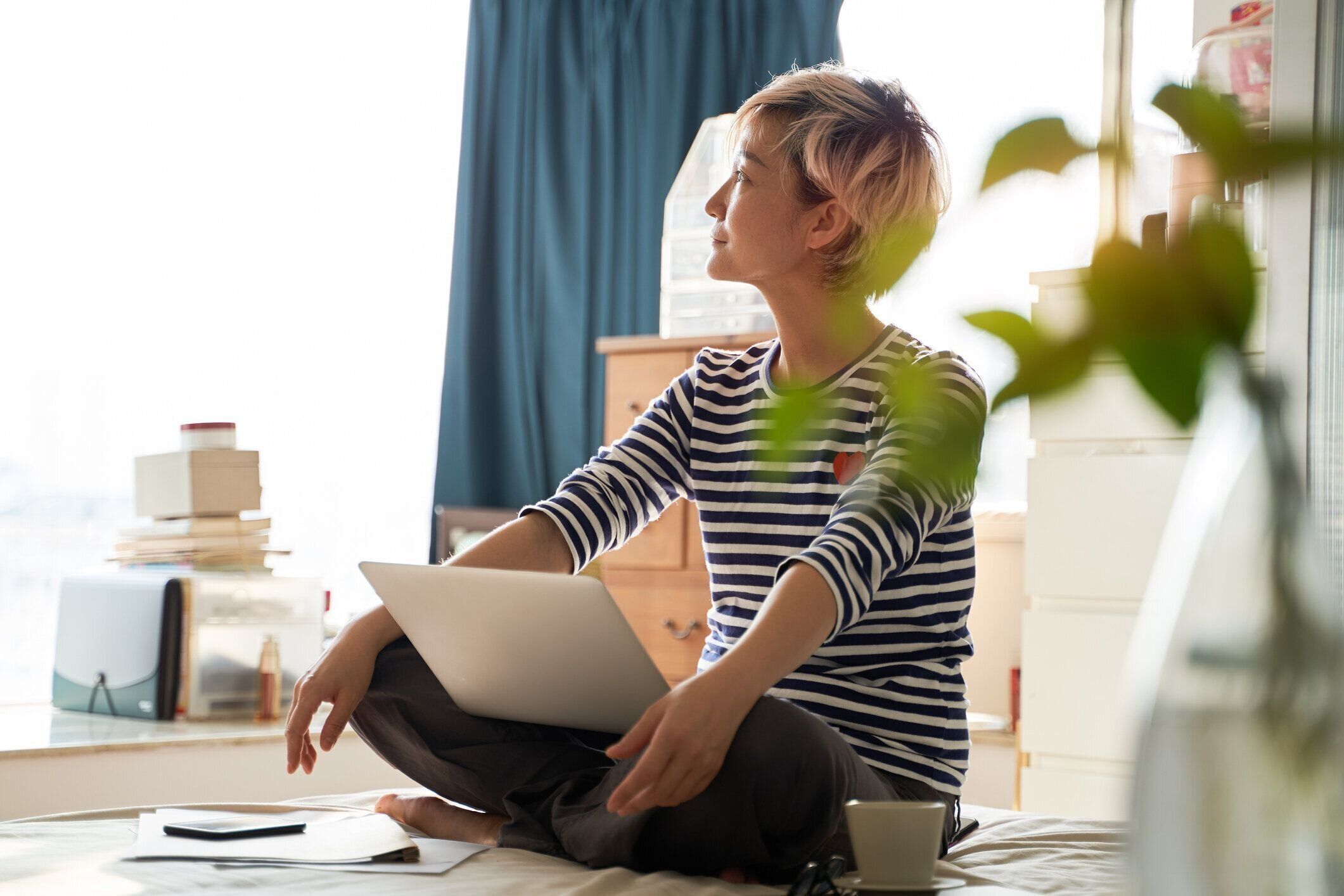 美しいアジアの女性はベッドの上に座って、ラップトップで自宅で働いています