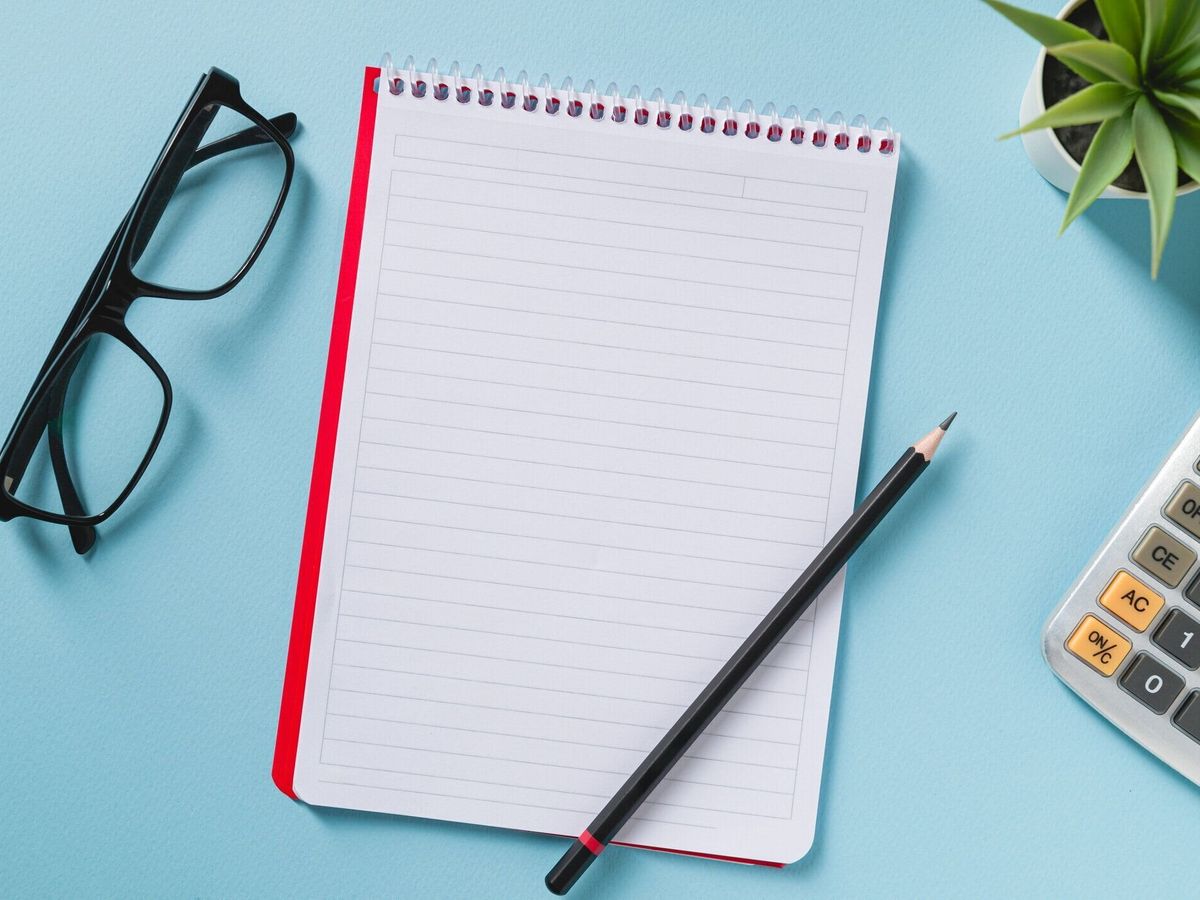 青いオフィスの机の上に空白のノートブック、メガネ、ペン、電卓、緑の植物の上から見た図