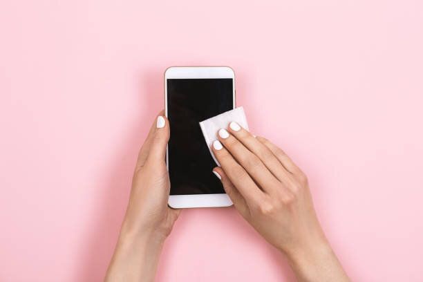 女性はスマートフォンの画面を消毒します。